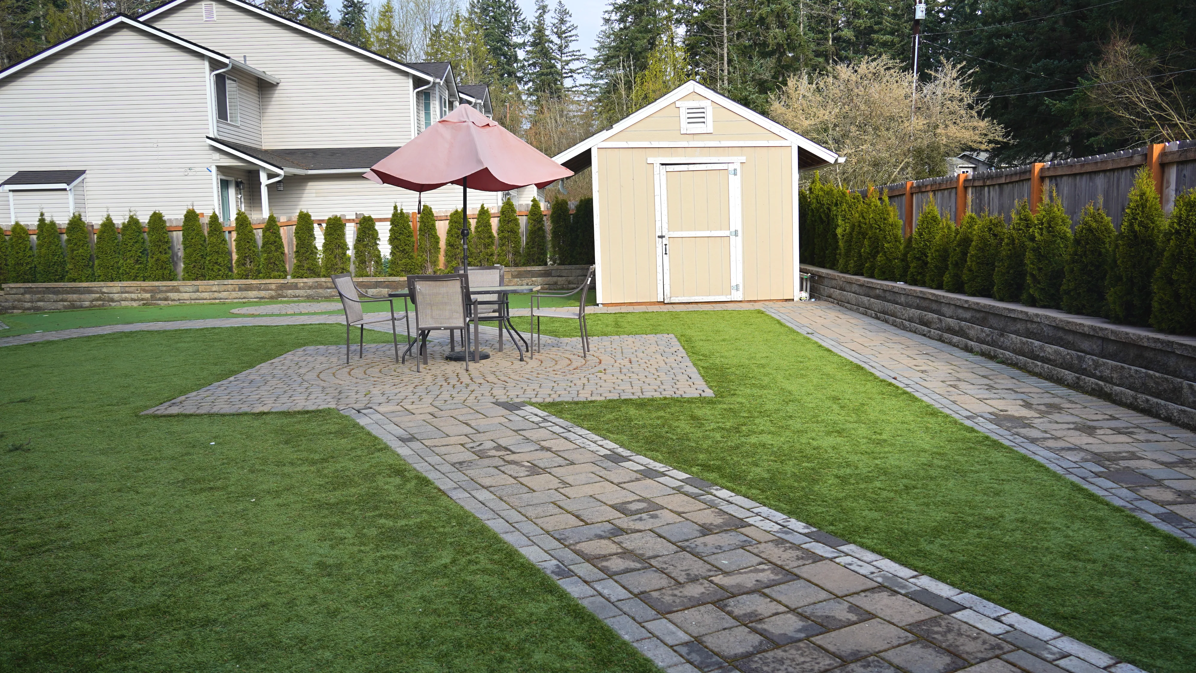 Landscaped backyard with paver patio, outdoor dining set, and garden shed
