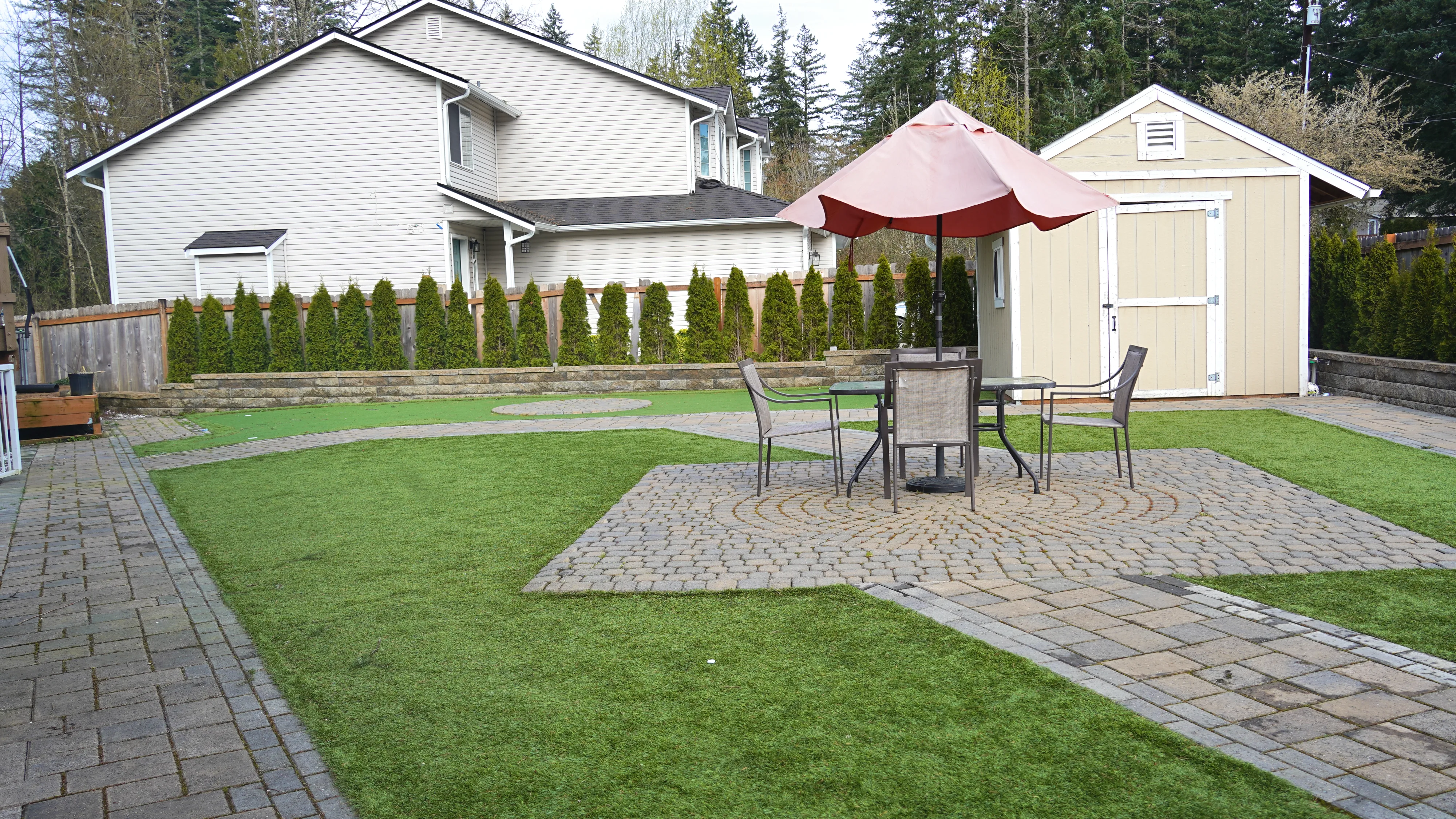 Backyard patio with umbrella, dining chairs, and manicured lawn