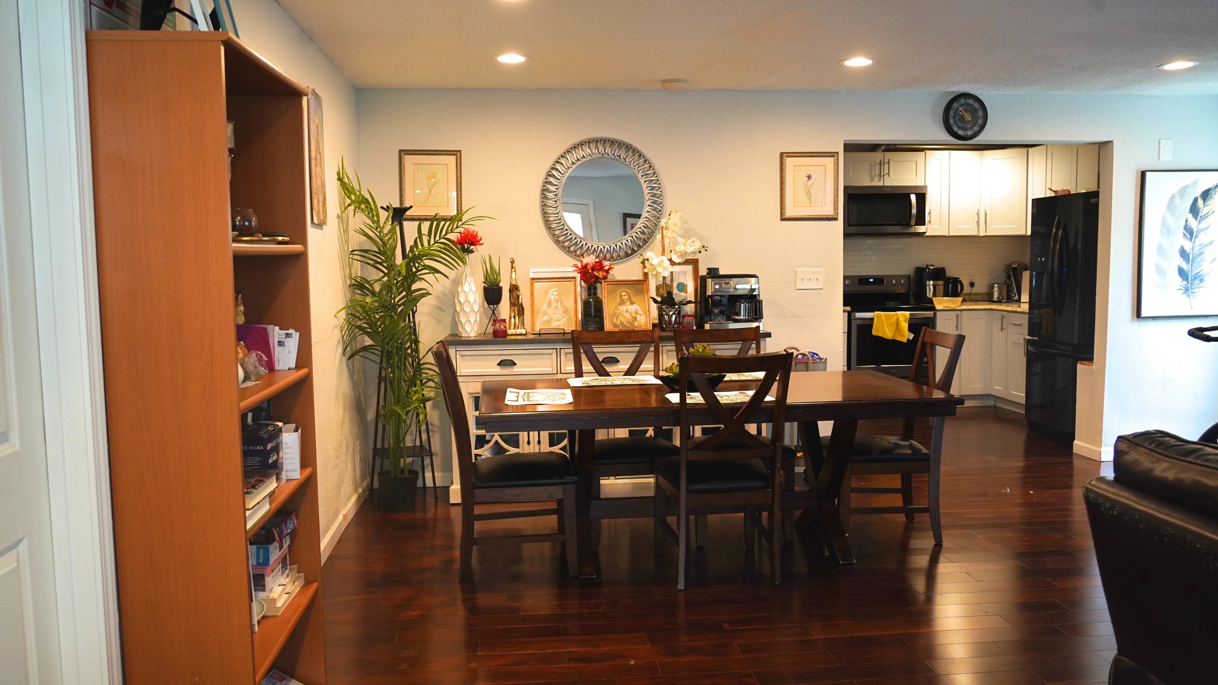 Dining area with wooden table, decorative mirror, and open kitchen