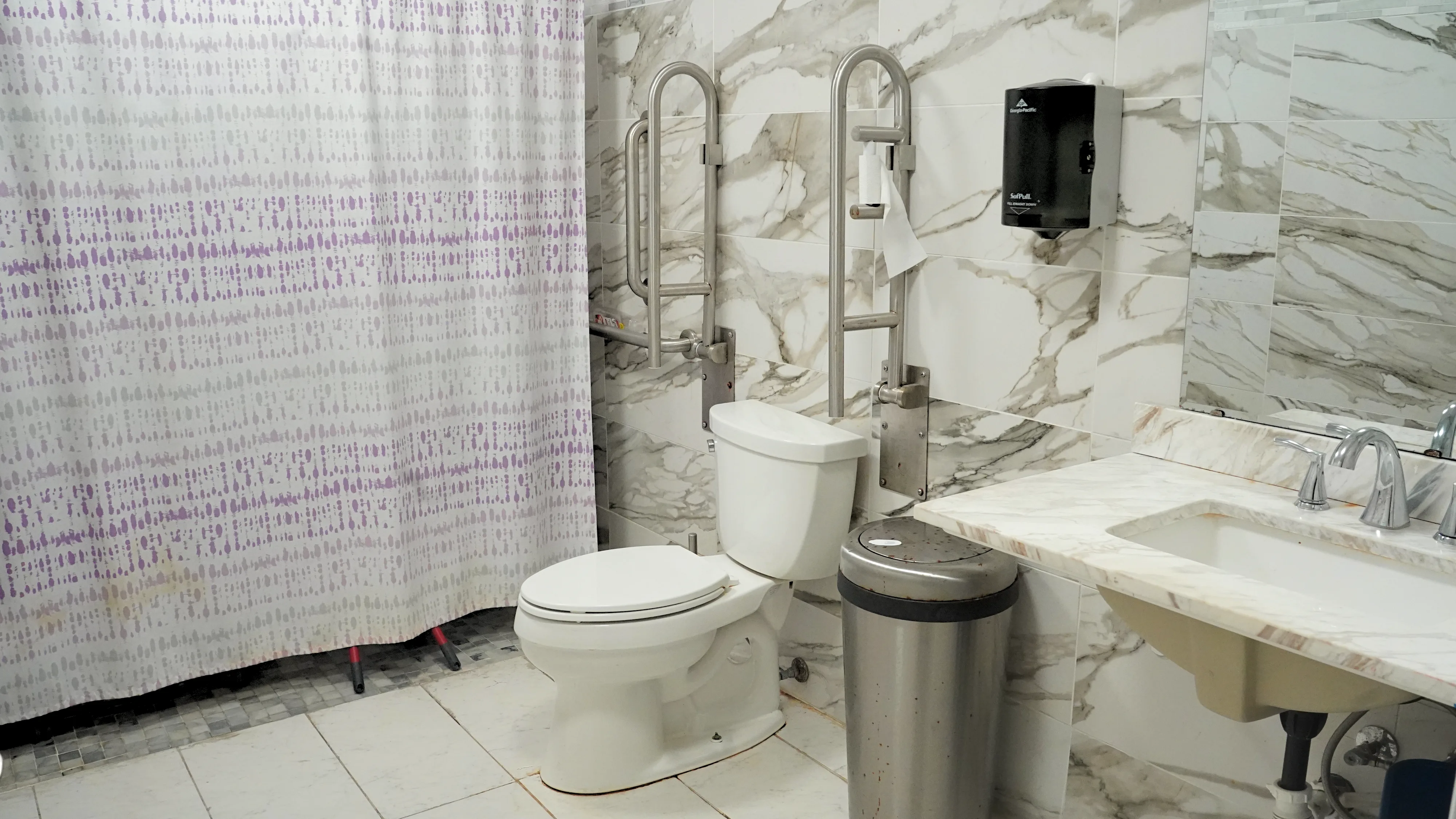 Accessible bathroom with marble tile walls and safety grab bars