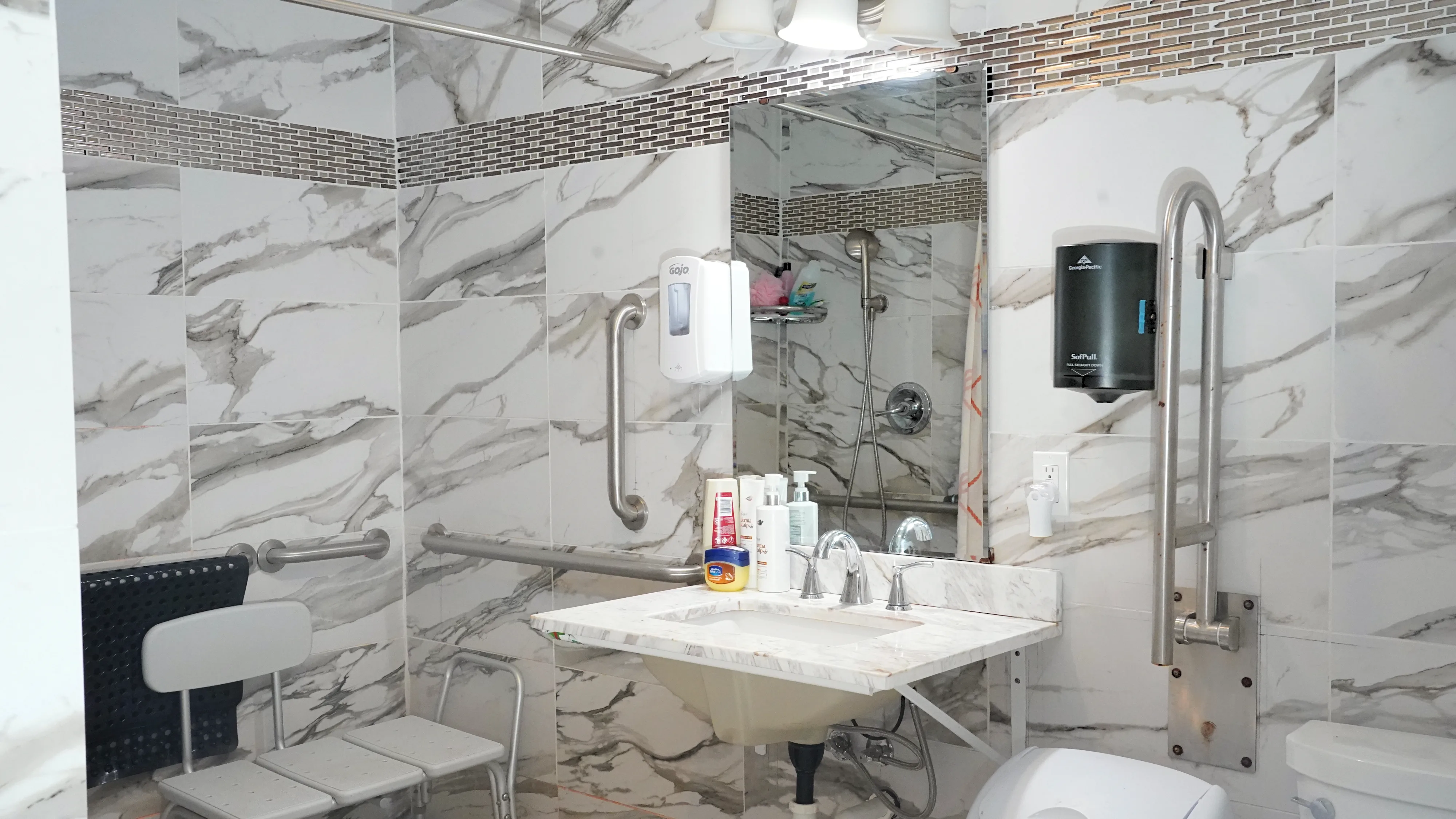 Accessible shower with transfer bench, grab bars, and marble tile