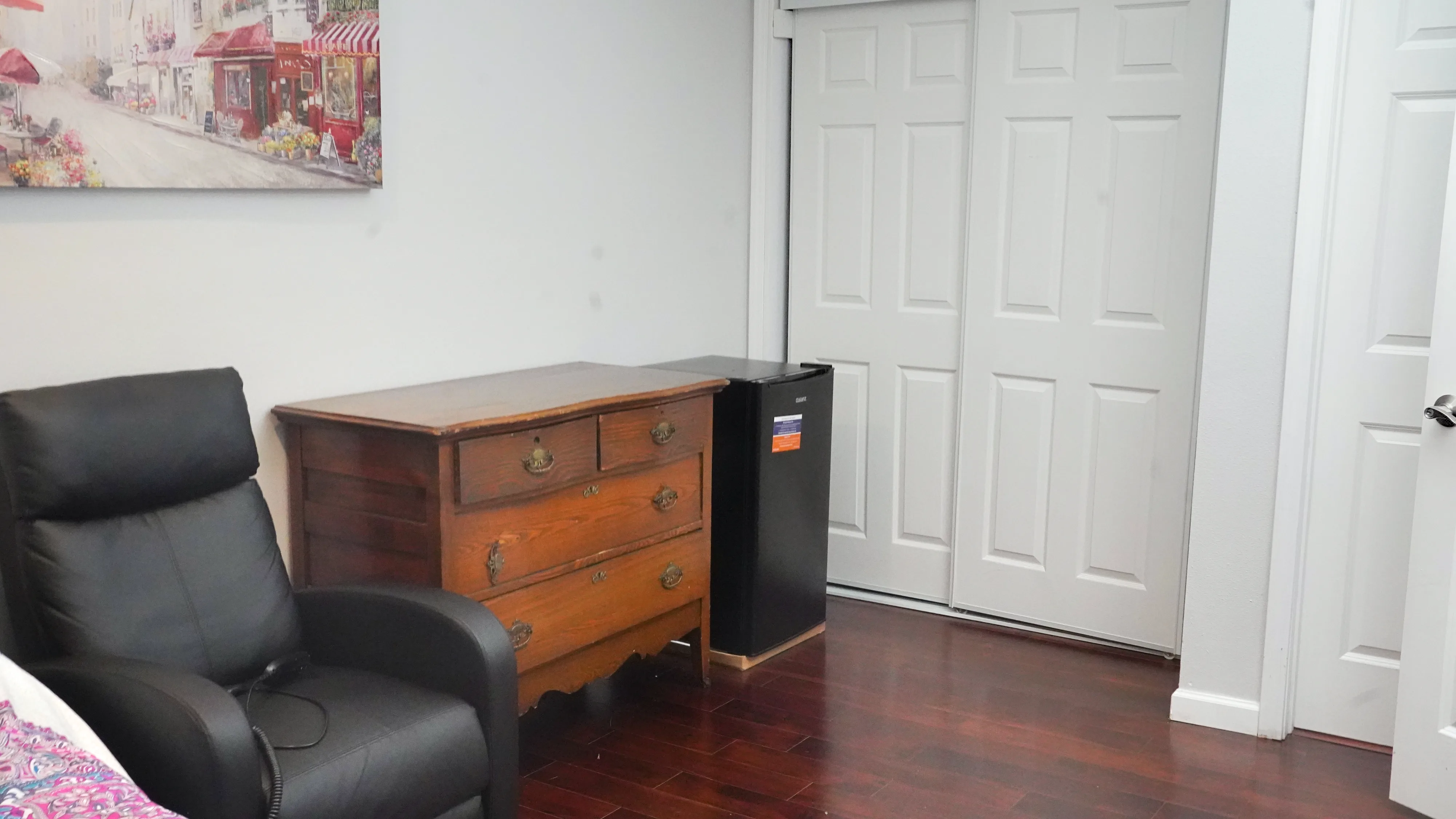Bedroom with recliner chair, dresser, mini fridge, and closet